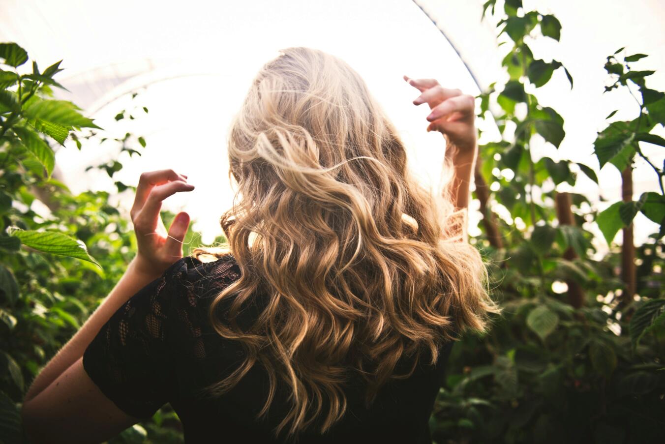 Woman with curly blonde hair walking by plants