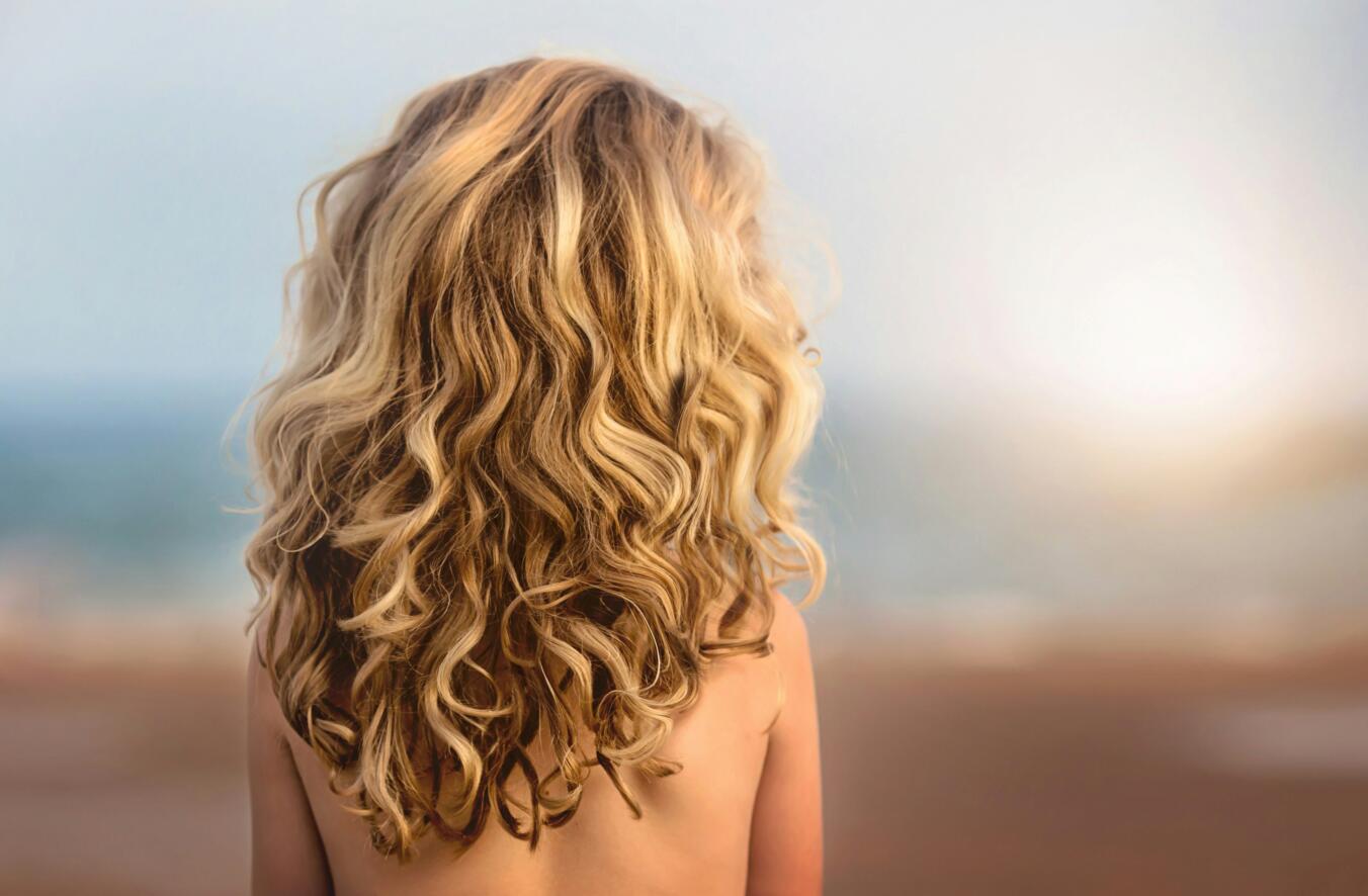 Young girl with thick, curly blonde hair facing away from the camera