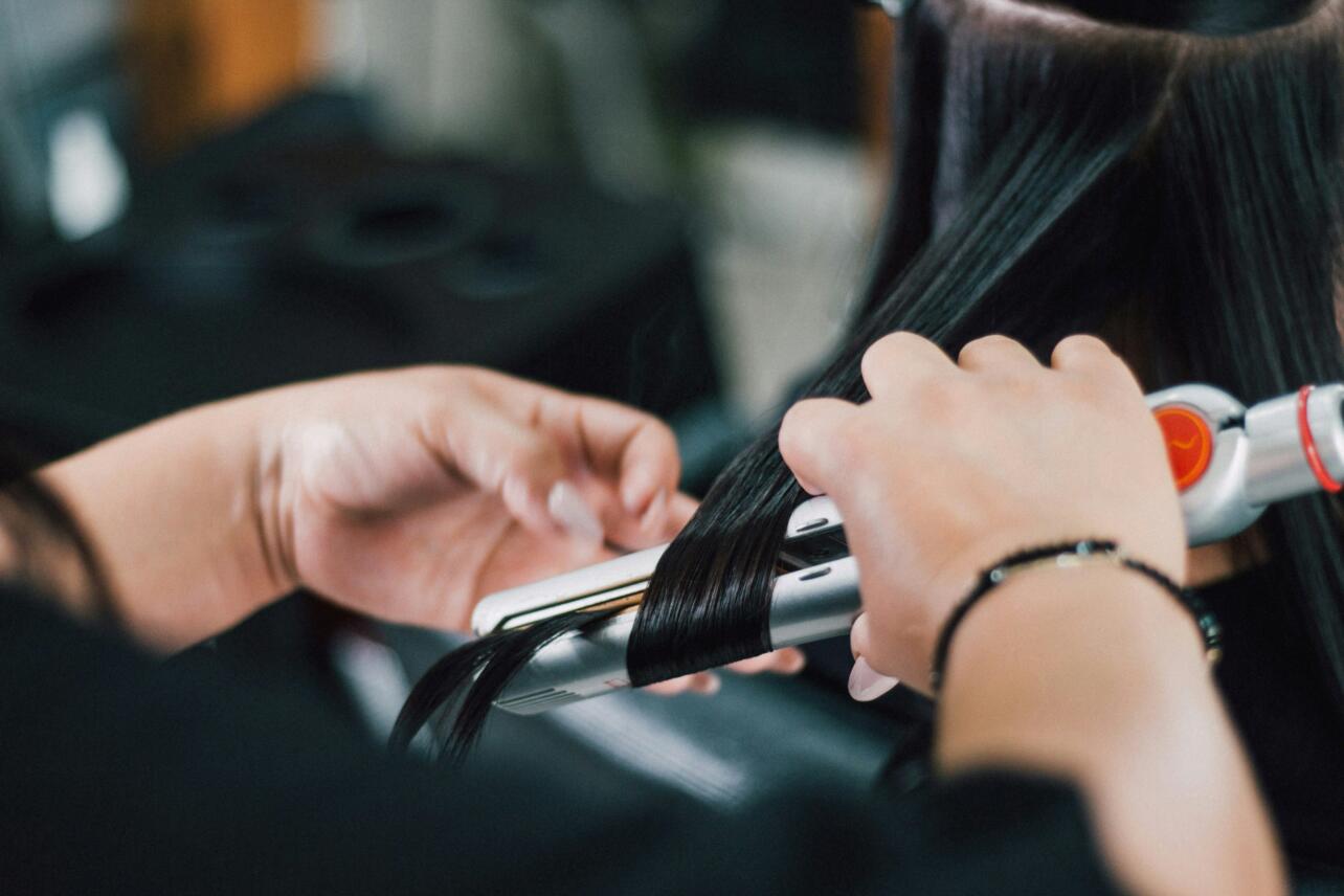 Stylist using hair straightener on woman's hair