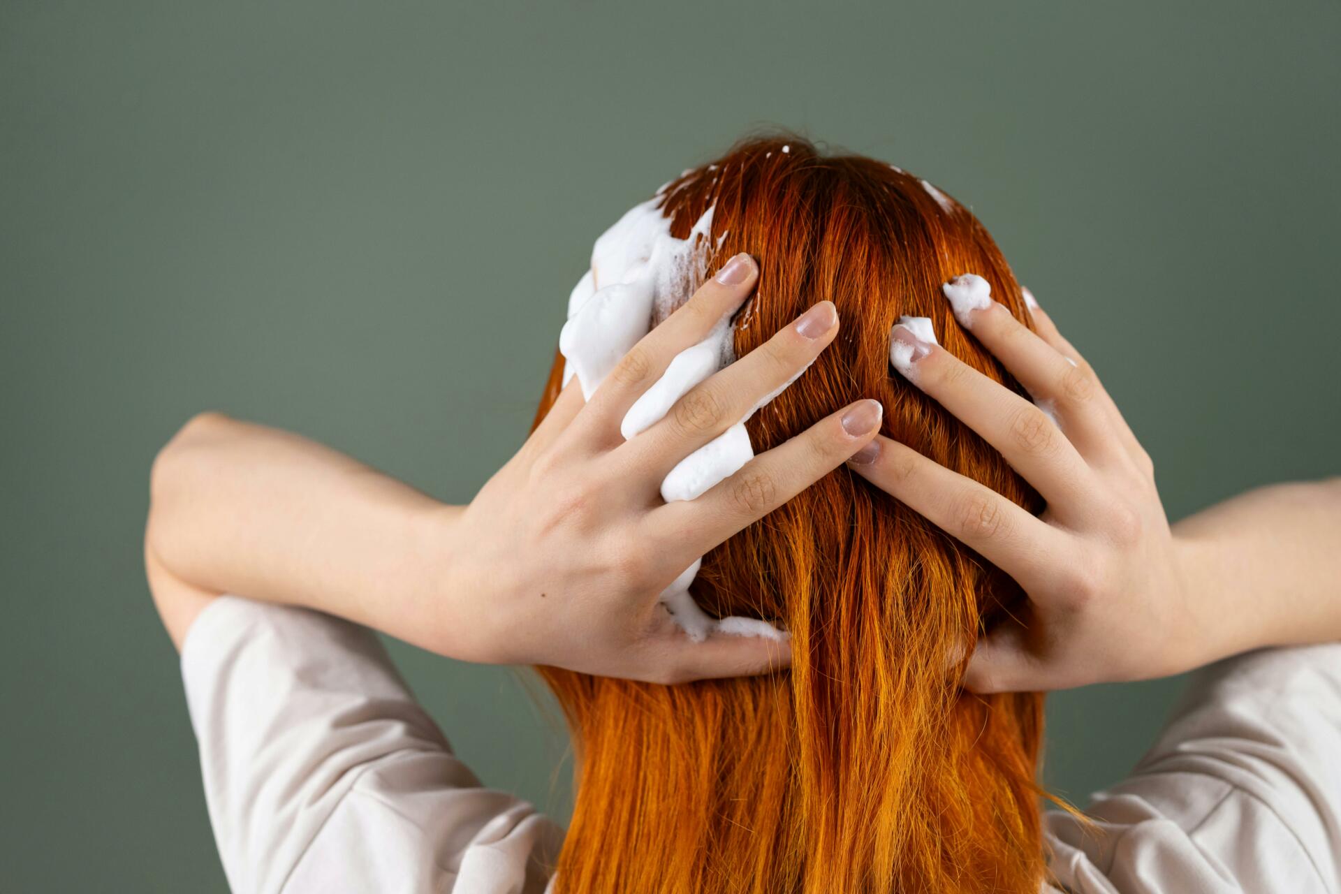 Woman with bright red hair applying a treatment at home